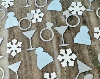 May include: Assortment of light blue and white paper confetti featuring snowflakes, martini glasses, rings, and winter hats.