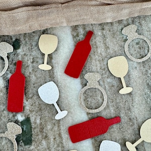 May include: A set of red and gold glitter party game pieces. The pieces are shaped like wine bottles, wine glasses, and engagement rings.
