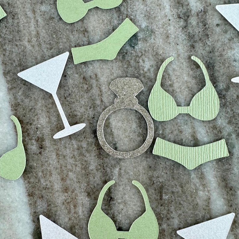 May include: A set of green and white paper cutouts for a bachelorette party. The cutouts include a ring, a martini glass, and a bikini.