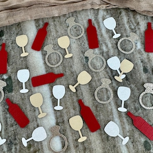 May include: Assortment of confetti featuring wine glasses, wine bottles, and engagement rings in red, white, and gold glitter.