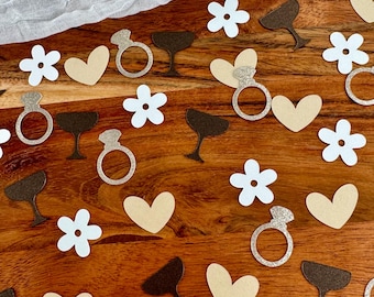 Puede incluir: Una variedad de formas de confeti en marrón, blanco y dorado. Las formas incluyen corazones, anillos, flores y copas de champán. El confeti es perfecto para una despedida de soltera o una boda.