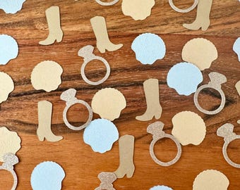 May include: A scattering of light blue and brown paper cutouts on a wooden surface. The cutouts include seashells, boots, and rings.