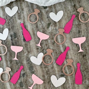 May include: Pink, white, and gold confetti with various shapes including hearts, champagne glasses, rings, and champagne bottles.