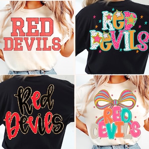 Puede incluir: Cuatro camisetas con el texto "RED DEVILS" en varios diseños. Una camiseta es de color crema con letras rojas en bloque. Otra es negra con un diseño colorido. Las otras dos camisetas son negras y crema con diferentes fuentes.