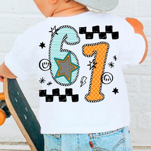 May include: White t-shirt featuring a vibrant '67' design. The number '6' is teal with a star, and the number '7' is orange. Black and white checkered patterns and star graphics surround the numbers. The shirt is worn by a person holding a skateboard.