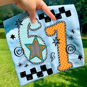 May include: Light blue fabric featuring the numbers 61 in a retro design. The number 6 is light blue with a checkered outline and a star in the center. The number 1 is orange with a checkered pattern. Additional graphics include stars, lightning bolts, and smiley faces.