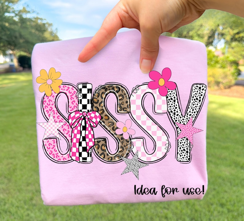 May include: A light pink t-shirt with the word "SASSY" in a playful, multi-patterned design. The letters feature leopard print, pink gingham, and black and white checkered patterns, accented with flower and star graphics. The text "Idea for use!" is printed below.