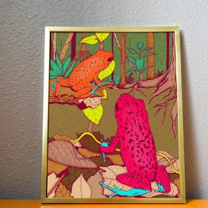 Peut inclure: Impression d'art encadrée représentant deux grenouilles stylisées dans une jungle. L'une est orange, l'autre rose vif. Le fond comprend un feuillage vert, des branches brunes et un cadre doré.