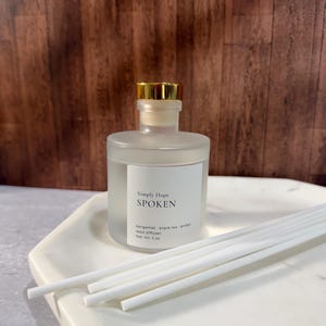May include: A frosted glass reed diffuser bottle with a gold cap and a white label reading Simply Hope SPOKEN bergamot black tea amber reed diffuser Net Wt 5 oz, accompanied by several white reed sticks.