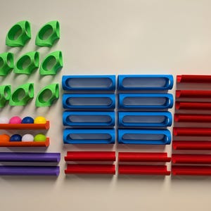 May include: A set of colorful plastic track pieces for a marble run game. The set includes green, blue, red, and purple pieces. There are also five colorful marbles.