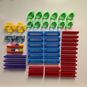 May include: A set of colorful plastic track pieces for a marble run. The set includes straight and curved track pieces in green, blue, red, purple, and yellow. There are also several cross-shaped pieces in yellow.