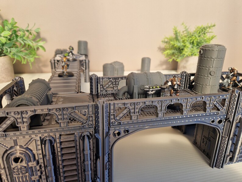 May include: A gray, metal, modular, sci-fi themed terrain set for tabletop gaming. The set features a bridge, a walkway, and a variety of pipes and other industrial details. The set is painted in a dark gray color and has a weathered look.