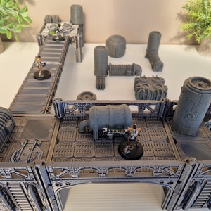 May include: A gray, industrial-themed tabletop gaming terrain set with multiple pieces, including a walkway, pipes, and a large cylindrical structure.  The set is designed for use with miniature figures and includes several figures.