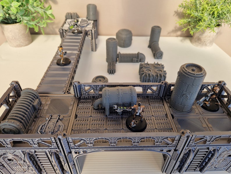 May include: A gray, industrial-themed tabletop gaming terrain set with multiple pieces, including a walkway, pipes, and a large cylindrical structure.  The set is designed for use with miniature figures and includes several figures.