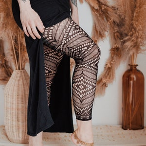 Peut inclure: Une personne portant un legging noir avec un motif de dentelle géométrique et une jupe noire. Elle porte des bracelets de cheville dorés et a des tatouages sur les jambes.