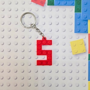 May include: Red plastic keychain shaped like the number 5. The keychain is attached to a silver key ring.