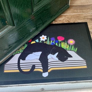 Floral Tuxedo Cat  Slim Door mat. Rubber backed non slip mat. Machine washable. Tuxedo Cat sleeping on book with  flowers.