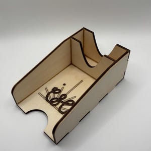 May include: A light-colored wooden desk organizer with a decorative laser-cut design. The organizer has a curved top and a compartment divider. The front features an ornate design with the letters "E" and "S".