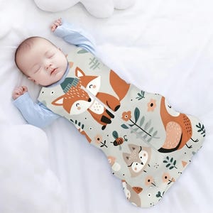 Puede incluir: Un saco de dormir para bebé gris y blanco con cierre de cremallera. El saco de dormir presenta un diseño de zorro, pájaro y abeja.