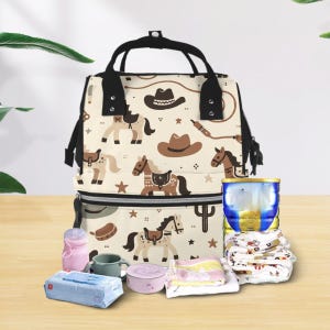 May include: A beige diaper bag with a black zipper and handles. The bag has a pattern of horses, cowboy hats, and stars. The bag is filled with baby supplies, including a bottle of formula, a diaper, and a small container.
