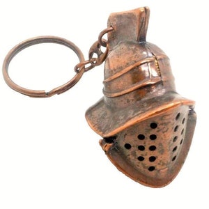 May include: A copper-colored gladiator helmet keychain with a key ring. The helmet has a detailed design with a visor and a plume on top.