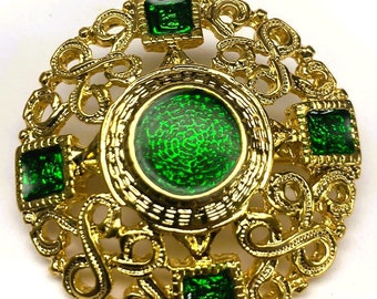 May include: A gold-toned brooch with a green enamel center and four smaller green enamel squares. The brooch is decorated with intricate gold filigree.