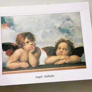 May include: A vintage print of two cherubs with wings, one with a hand on their chin and the other with their arms crossed. The print is titled "Angeli - Raffaello".