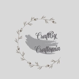 May include: A logo design with the text "CraftBy Craftopia" in a gray brushstroke style, surrounded by a wreath of stylized leaves and flowers.