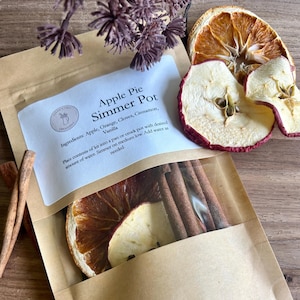 May include: A brown paper bag with a label that reads "Apple Pie Simmer Pot". The bag contains dried apple slices, orange slices, cinnamon sticks, and cloves. The ingredients are for making a simmer pot, which is a type of potpourri that is simmered on the stovetop to create a pleasant aroma.