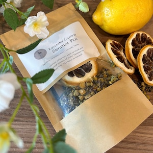 Puede incluir: Una bolsa de papel marrón con una ventana transparente que muestra lavanda, limón y manzanilla secos en su interior. La bolsa tiene una etiqueta blanca que dice "Lavender Garden Simmer Pot" y enumera los ingredientes: lavanda, limón, manzanilla, vainilla. La etiqueta también incluye instrucciones de uso: "Coloque el contenido del kit en una olla o olla de cocción lenta. Cantidad de agua deseada. Cocine a fuego lento. Agregue agua según sea necesario."