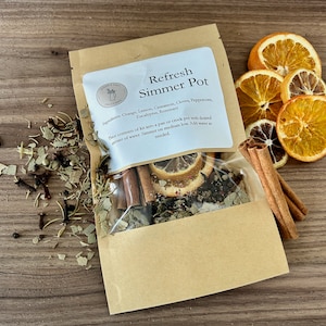 May include: A brown paper pouch with a white label that reads "Refresh Simmer Pot" and lists the ingredients: Orange, Lemon, Cinnamon, Cloves, Peppercorn, Eucalyptus, Rosemary. The pouch contains a mix of dried herbs, spices, and citrus fruit slices.