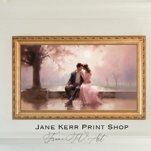 May include: A framed painting of a couple sitting on a stone wall in a park. The woman is wearing a pink dress and the man is wearing a suit. The painting is set against a backdrop of trees and a pink sky. The frame is gold and has a decorative design. The text "JANE KERR PRINT SHOP Frame Itv Art" is below the painting.