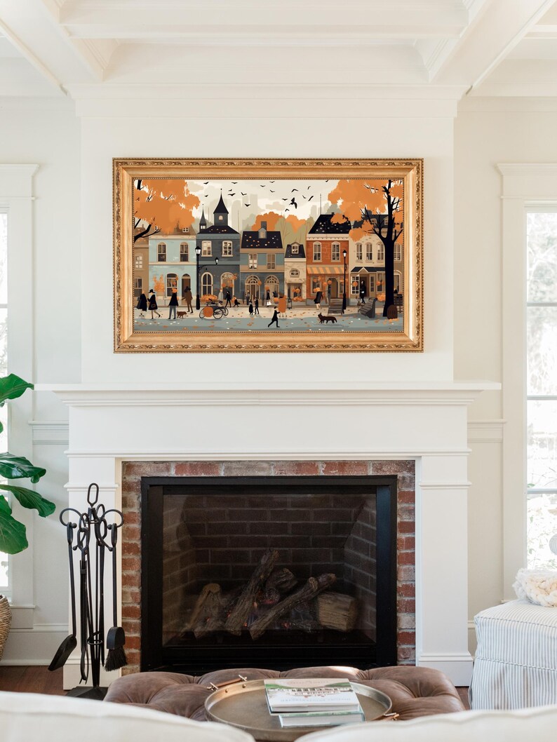 May include: A framed illustration of a quaint town street scene with colorful buildings, trees, and people walking. The illustration is in a gold frame and hangs above a fireplace.