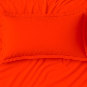 Pode incluir: Uma almofada laranja vibrante sobre um lençol a condizer. A almofada é retangular com uma borda costurada. O tecido parece macio e liso, com rugas subtis no lençol. O esquema de cores geral é um laranja brilhante sólido.