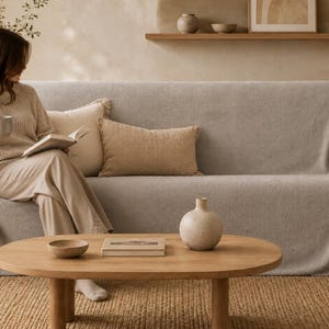Könnte beinhalten: Ein hellbeiger Sofabezug, der über ein Sofa drapiert ist und einen weichen, strukturierten Stoff aufweist. Der Bezug erstreckt sich über die Armlehnen und die Rückenlehne und bietet eine neutrale, einfarbige Schicht.