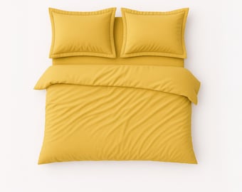 May include: A top-down view of a bed with a mustard-yellow duvet cover and two matching pillowcases. The bedding is neatly arranged on a white background, creating a clean and inviting aesthetic. The pillowcases have a subtle border.