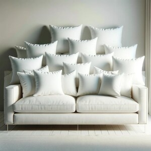 May include: A white sofa with numerous white square and rectangular pillows arranged on the backrest. The sofa has a minimalist design with a light-colored fabric and thin metal legs. The pillows create a layered, comfortable appearance.