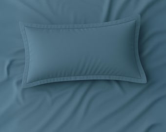 May include: A teal pillow with a decorative border sits on a matching teal bedsheet. The pillow is rectangular with a subtle, stitched edge. The fabric appears smooth and slightly creased, suggesting a soft texture. The overall theme is bedding.