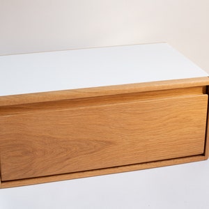 May include: A white top with a drawer made of light brown wood. The drawer is open and the wood grain is visible.