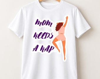 Puede incluir: Una camiseta blanca de manga corta con un estampado gráfico de una persona con cabello castaño rizado que viste una blusa y pantalones cortos de color rosa claro, en posición reclinada. El texto "MOM NEEDS A NAP" está en letra cursiva morada.