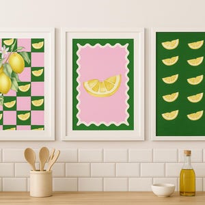 May include: Three framed art prints featuring lemon-themed designs. One print showcases lemons on a pink and green checkered background. Another has a lemon slice on a pink background with a green border. The third print displays lemon slices on a green background.