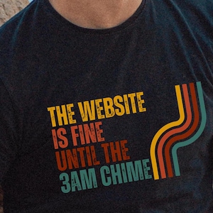 May include: Black t-shirt with a retro-style graphic that says "The website is fine until the 3AM chime".