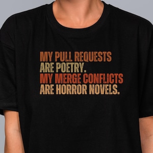 Op de afbeelding: Zwart T-shirt met de tekst "MY PULL REQUESTS ARE POETRY. MY MERGE CONFLICTS ARE HORROR NOVELS."
