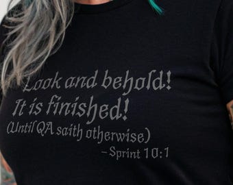 May include: A black t-shirt with the text "Look and behold! It is finished! (Until QA saith otherwise) - Sprint 10:1". The shirt is worn by a person with colorful hair and tattoos. The image also includes the text "Unique Geek".