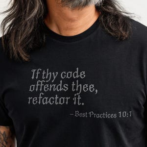 Op de afbeelding: Zwart T-shirt met de tekst "If thy code offends thee, refactor it." in een gestileerd lettertype. De zin "- Best Practices 10:1" staat eronder. Een "Unique Geek" logo is rechtsboven zichtbaar.