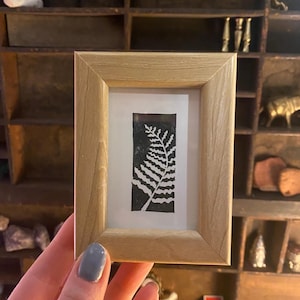 May include: A framed black and white print of a fern leaf in a light wood frame.
