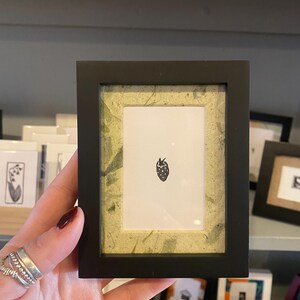 May include: A small black picture frame with a green mat and a simple black and white illustration of a strawberry inside.