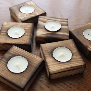 May include: Six wooden candle holders with a rustic finish. Each holder has a circular depression to hold a tea light candle.