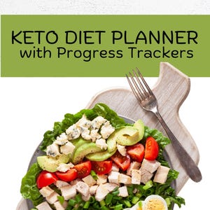 Op de afbeelding: Een keto-dieet salade met romaine sla, avocado, cherrytomaatjes, kip, blauwe kaas, spek, hardgekookte eieren en lente-uitjes. De salade is op een grijs bord en een houten snijplank met een zilveren vork.