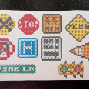 May include: A sheet of stickers with various traffic signs, including a stop sign, a yield sign, a one-way sign, a crosswalk sign, a hospital sign, a construction sign, a traffic light, and a sign that says "PINE LN".